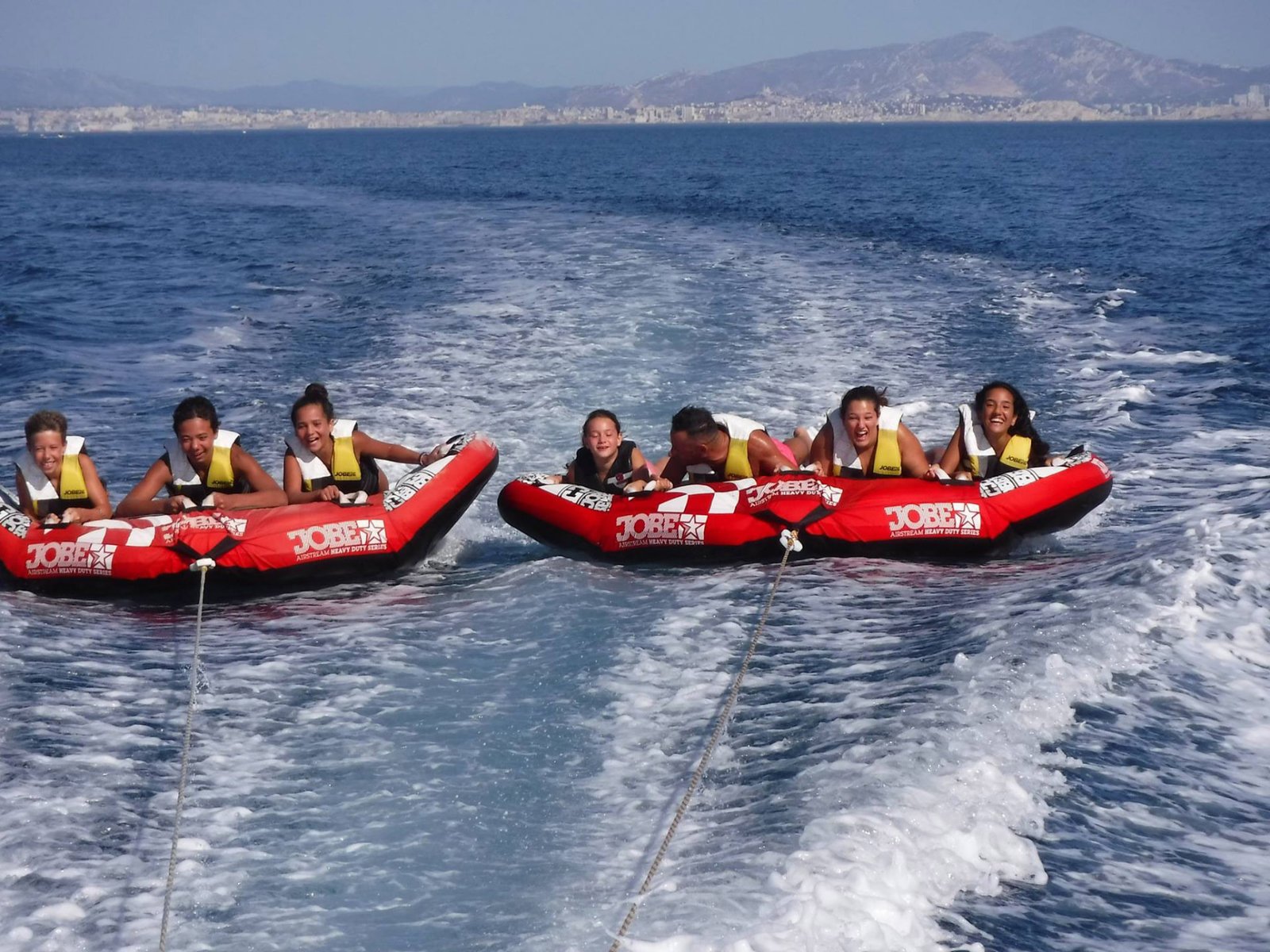 Amis riant sur une bouée tractée banana dans une mer turquoise